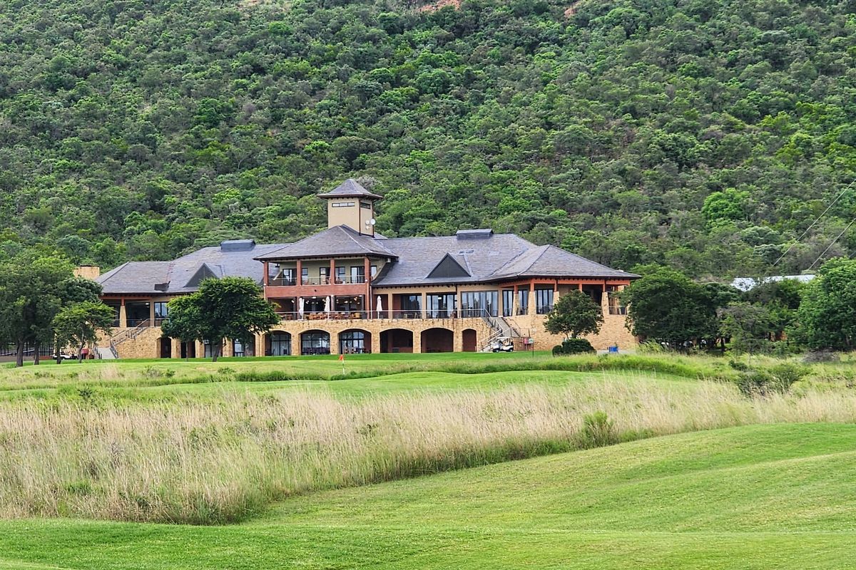A view of a large, well-maintained clubhouse facility situated on a golf course with a mountain backdrop.