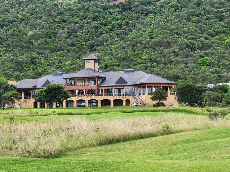 A view of a large, well-maintained clubhouse facility situated on a golf course with a mountain backdrop.