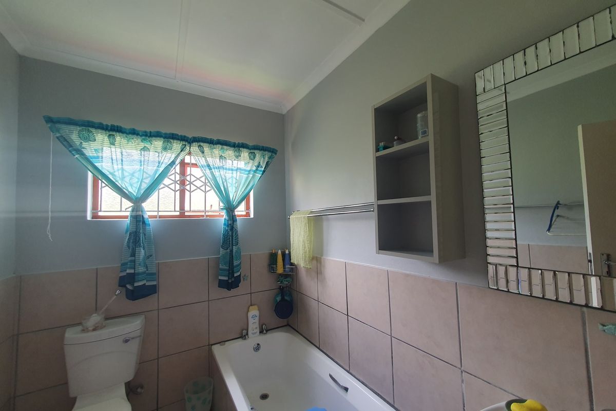 A functional bathroom featuring a built-in bathtub, toilet, and wall-mounted storage shelving with neutral wall tiling.