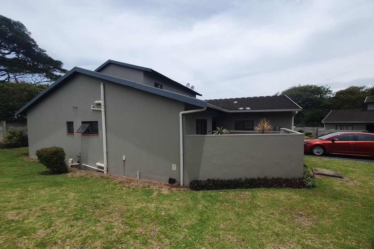 Rear view of the townhouse featuring plastered exterior walls, a tiled roof, and a private garden area with a boundary wall.