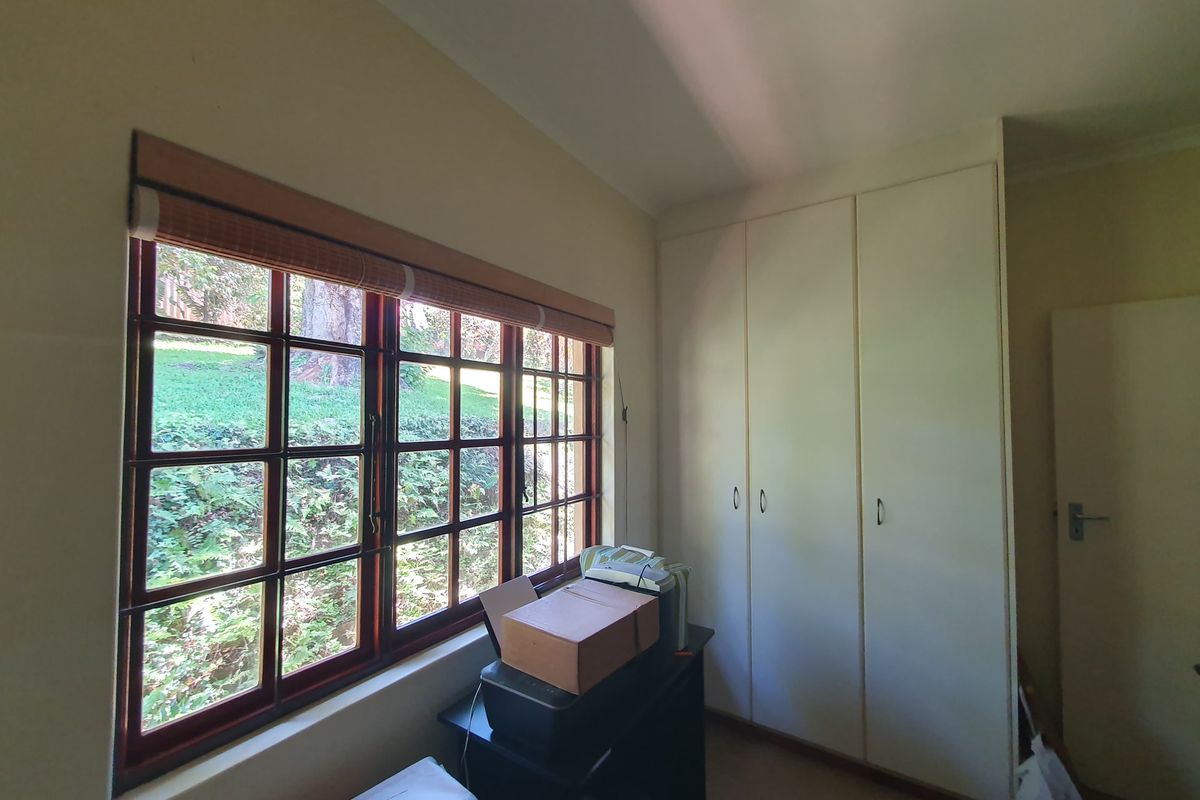 A bedroom featuring built-in cupboards and timber-framed windows overlooking a garden area.
