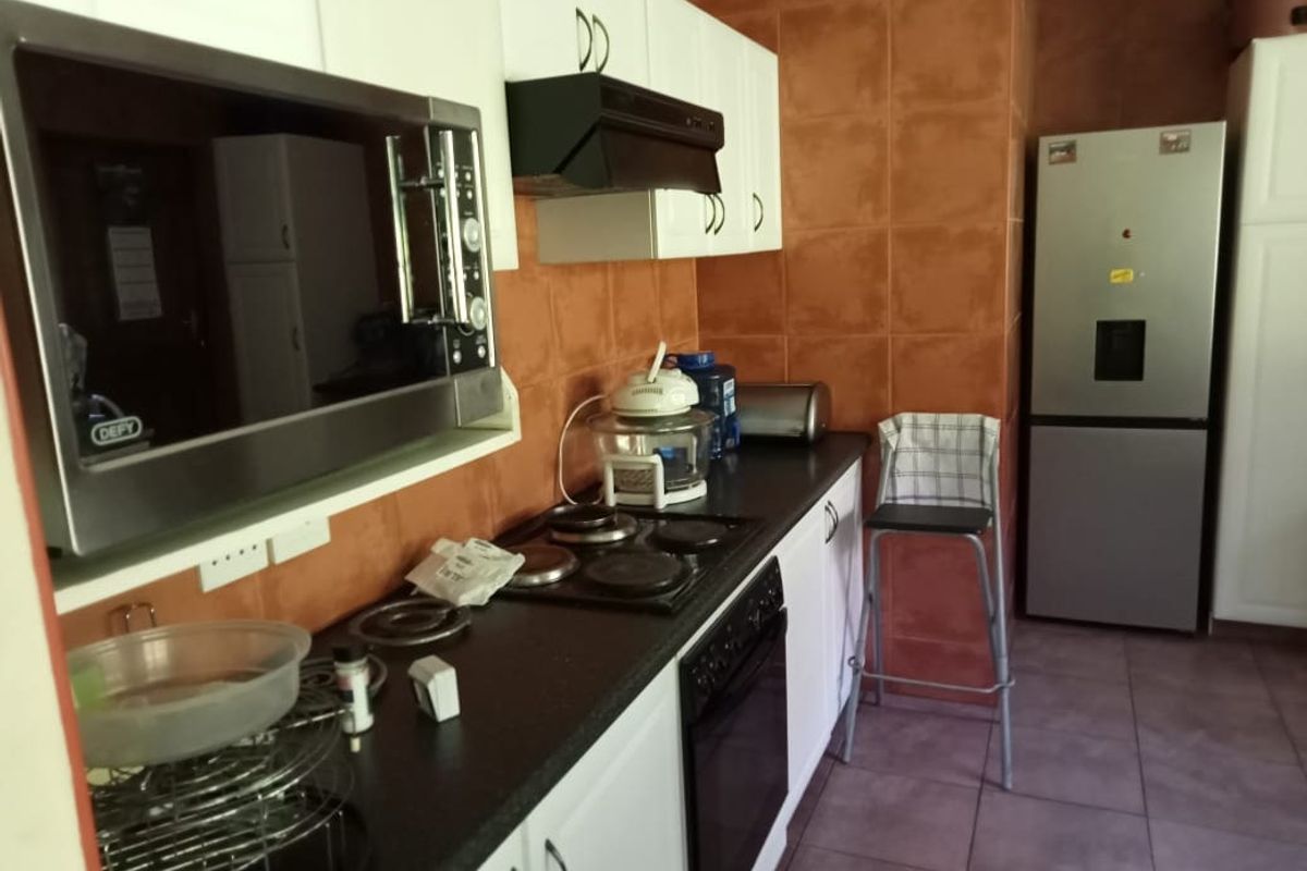 A functional kitchen featuring built-in cabinetry, an electric hob with extractor fan, built-in oven, microwave, and tiled finishes throughout.