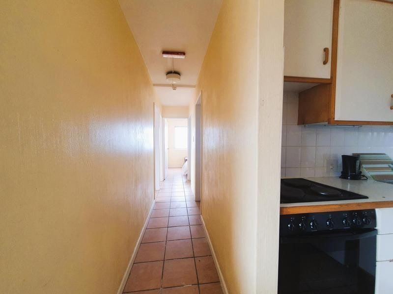 A narrow hallway leading to interior rooms, adjacent to a compact kitchen area featuring built-in cabinetry and an electric stove.