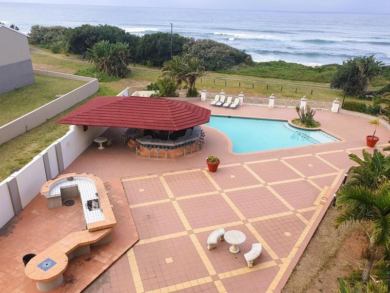 Aerial view of a communal pool area featuring a built-in bar, braai facilities, and tiled patio overlooking the ocean.