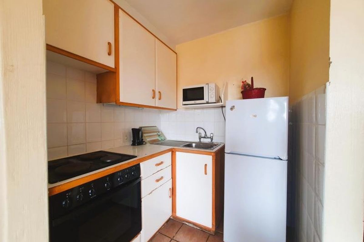 A compact, functional kitchen featuring built-in cabinetry, an electric stove with oven, stainless steel sink, and tiled backsplash.