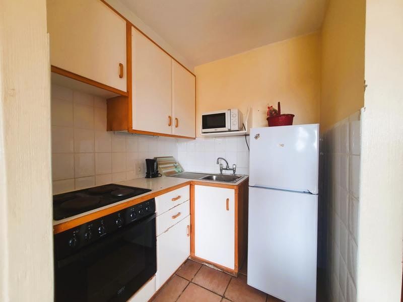 A compact, functional kitchen featuring built-in cabinetry, an electric stove with oven, stainless steel sink, and tiled backsplash.