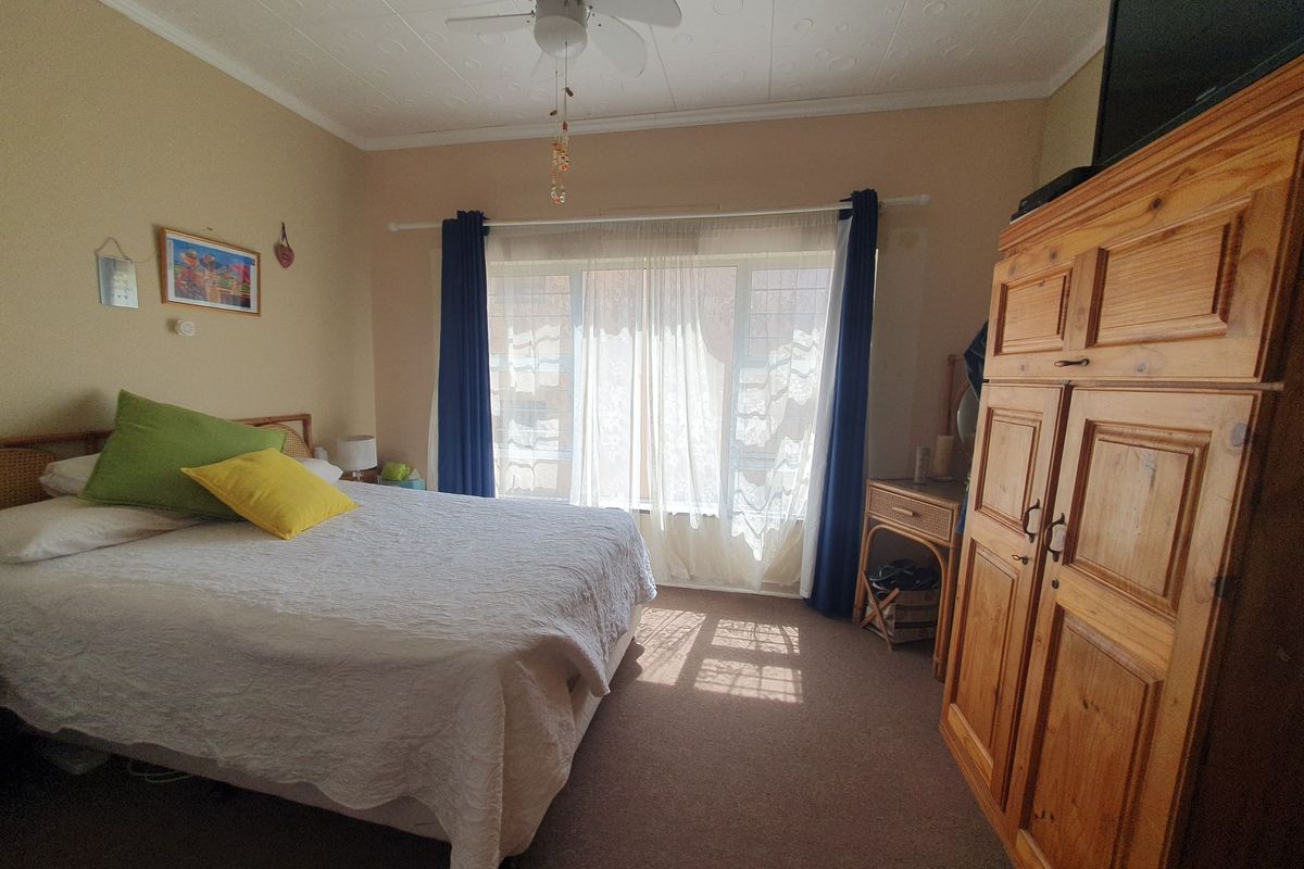 A bedroom featuring carpet flooring, a ceiling fan, and a textured ceiling, with natural light entering through a large window.