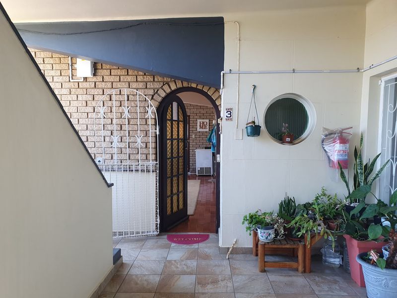 A covered apartment entrance featuring brickwork accents, a security gate, tiled flooring, and a distinctive circular window.