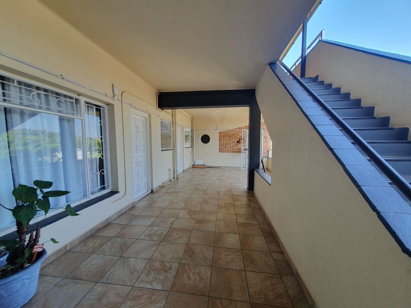 A spacious covered balcony or walkway featuring tiled flooring, a staircase, and secure access points to the apartment units.