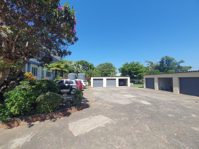 Exterior view of a residential apartment complex featuring multiple garage units and a paved driveway area with mature landscaping.