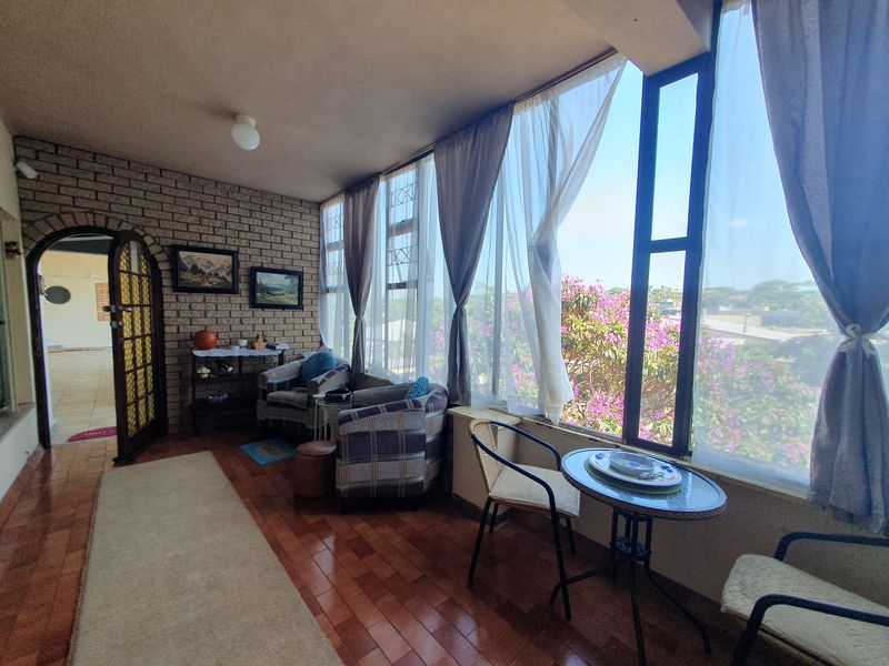 Enclosed balcony featuring exposed brick walls, tiled flooring, and large windows providing natural light and views of the surrounding area.