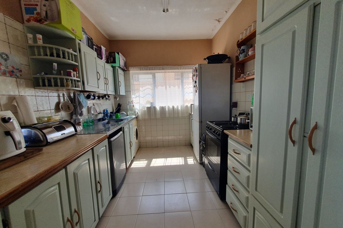 A functional galley-style kitchen featuring fitted cabinetry, tiled flooring, a double sink, and a freestanding stove, with potential for cosmetic modernization.