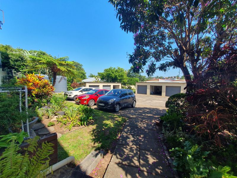 A view of the rear exterior area featuring a paved driveway, multiple lock-up garages, and a well-maintained landscaped garden.