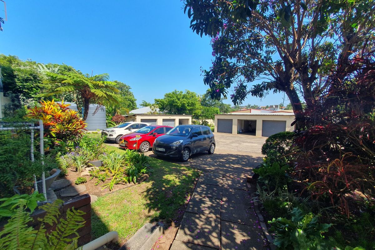 A view of the rear exterior area featuring a paved driveway, multiple lock-up garages, and a well-maintained landscaped garden.
