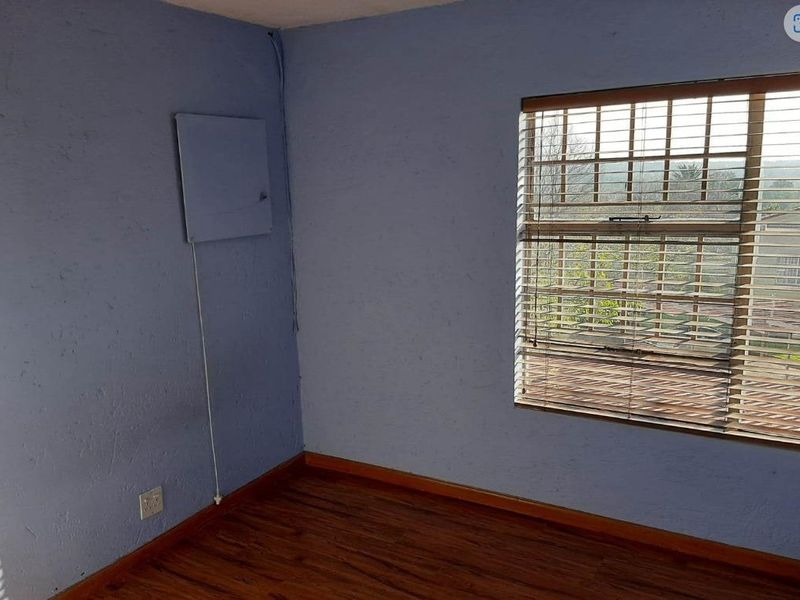 A vacant bedroom featuring wood-look flooring, a large window with fitted blinds, and blue textured walls with an exposed electrical panel.