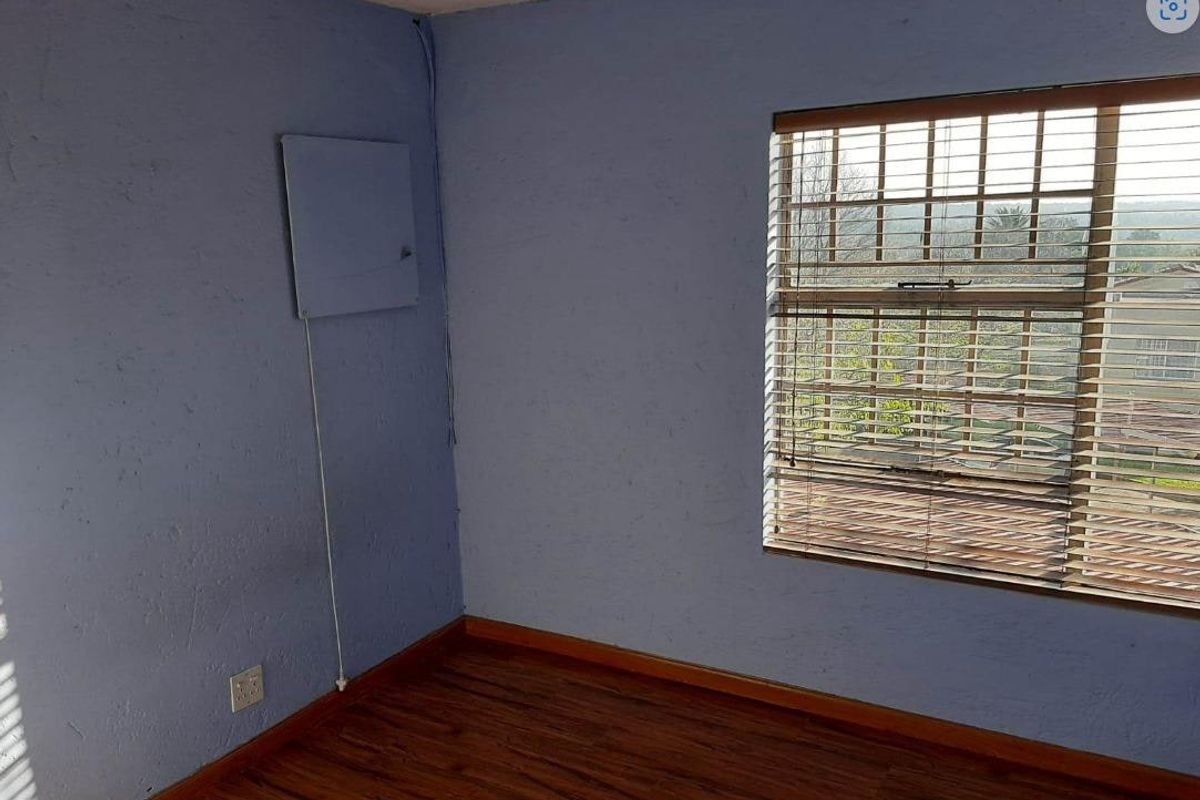 A vacant bedroom featuring wood-look flooring, a large window with fitted blinds, and blue textured walls with an exposed electrical panel.