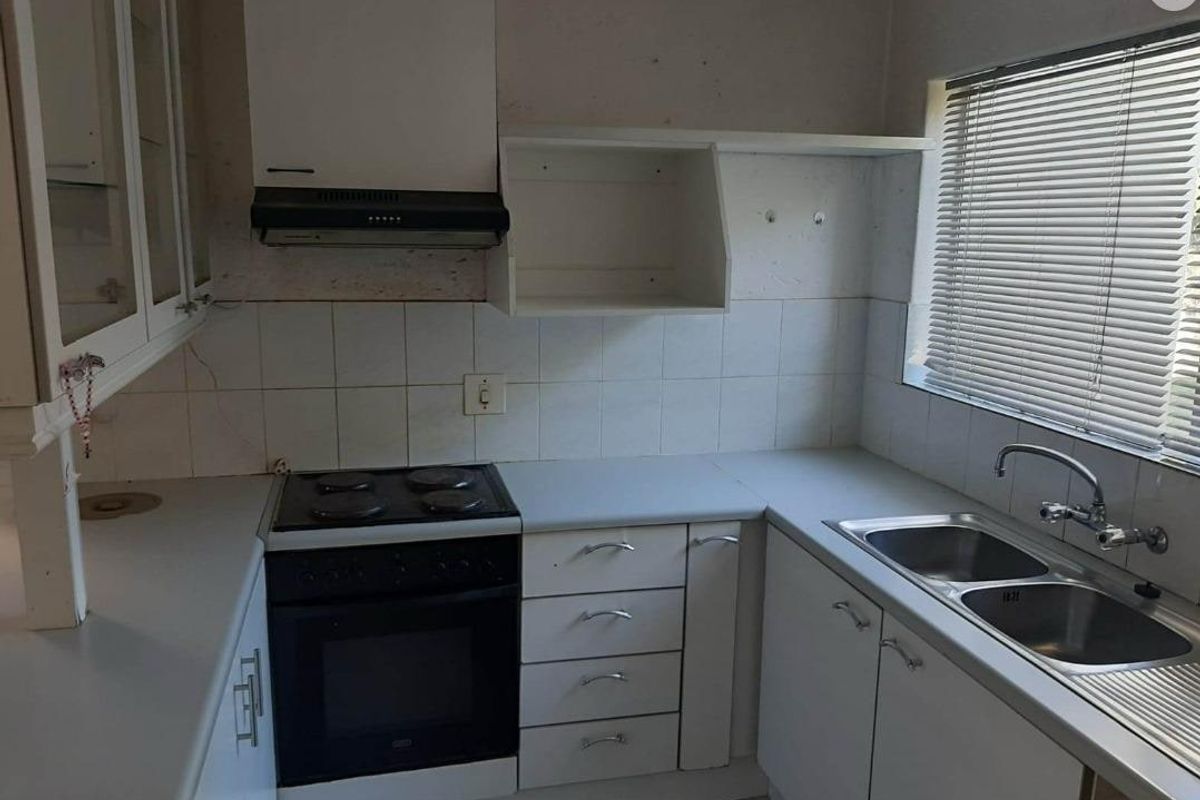 A dated kitchen featuring white cabinetry, a built-in electric stove with extractor fan, and a double stainless steel sink under a window.