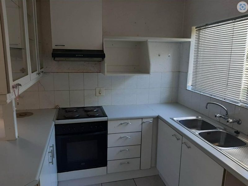 A dated kitchen featuring white cabinetry, a built-in electric stove with extractor fan, and a double stainless steel sink under a window.