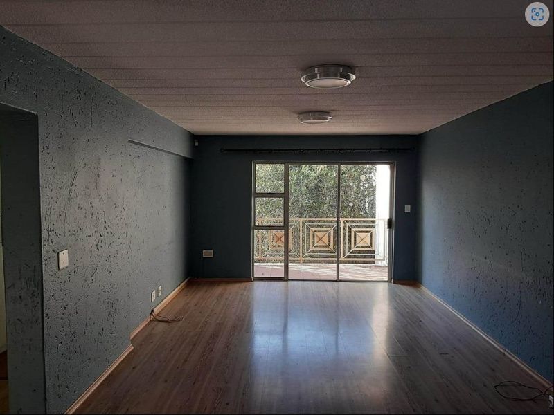 Spacious living area featuring laminate flooring, textured walls, and sliding glass doors leading to a private balcony.