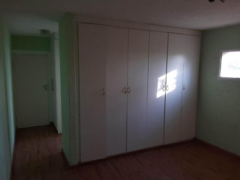 A bedroom featuring built-in floor-to-ceiling wardrobes, laminate flooring, and a small window, providing functional storage space.