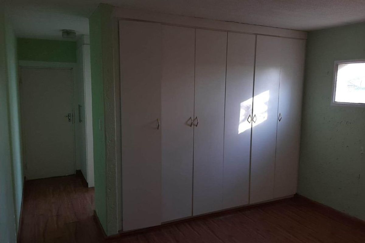 A bedroom featuring built-in floor-to-ceiling wardrobes, laminate flooring, and a small window, providing functional storage space.