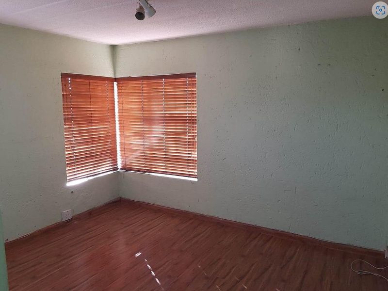An empty bedroom featuring wood-look laminate flooring, textured walls, and corner windows fitted with wooden blinds.