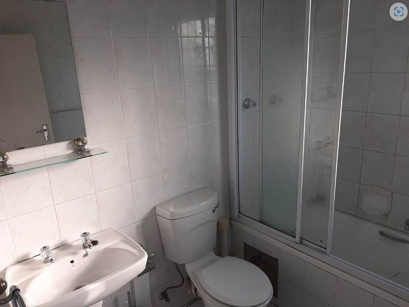 A functional bathroom featuring a pedestal basin, a toilet, and a shower-over-bath combination with sliding glass doors and full-height wall tiling.