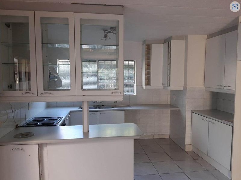 A functional kitchen featuring white cabinetry, built-in electric hob, double sink, and tiled flooring, offering a clean and practical layout.