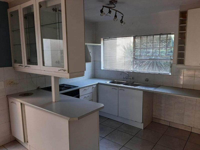 A dated kitchen featuring white cabinetry, a double basin sink, tiled flooring, and a built-in electric hob, offering a functional layout for renovation.