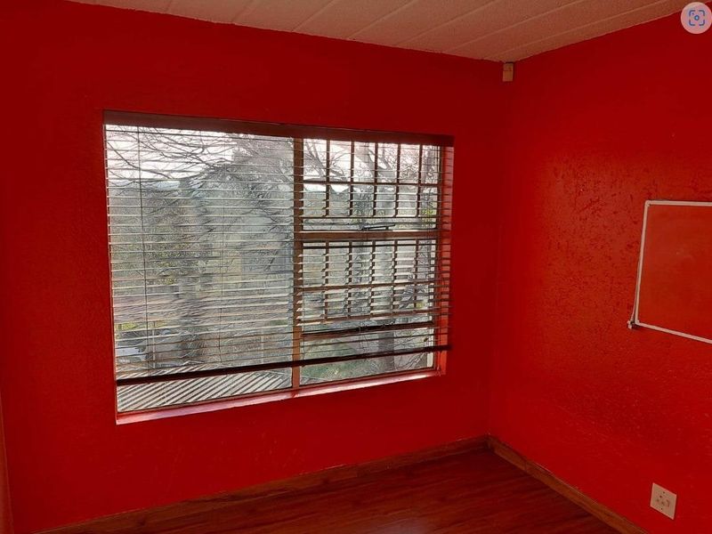 A bedroom featuring dark wood-look flooring and a large window with fitted blinds, finished with bold red wall paint.