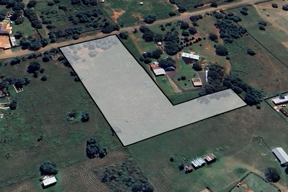 An aerial view of a vacant residential plot with boundary lines highlighted, situated in a semi-rural neighborhood setting.