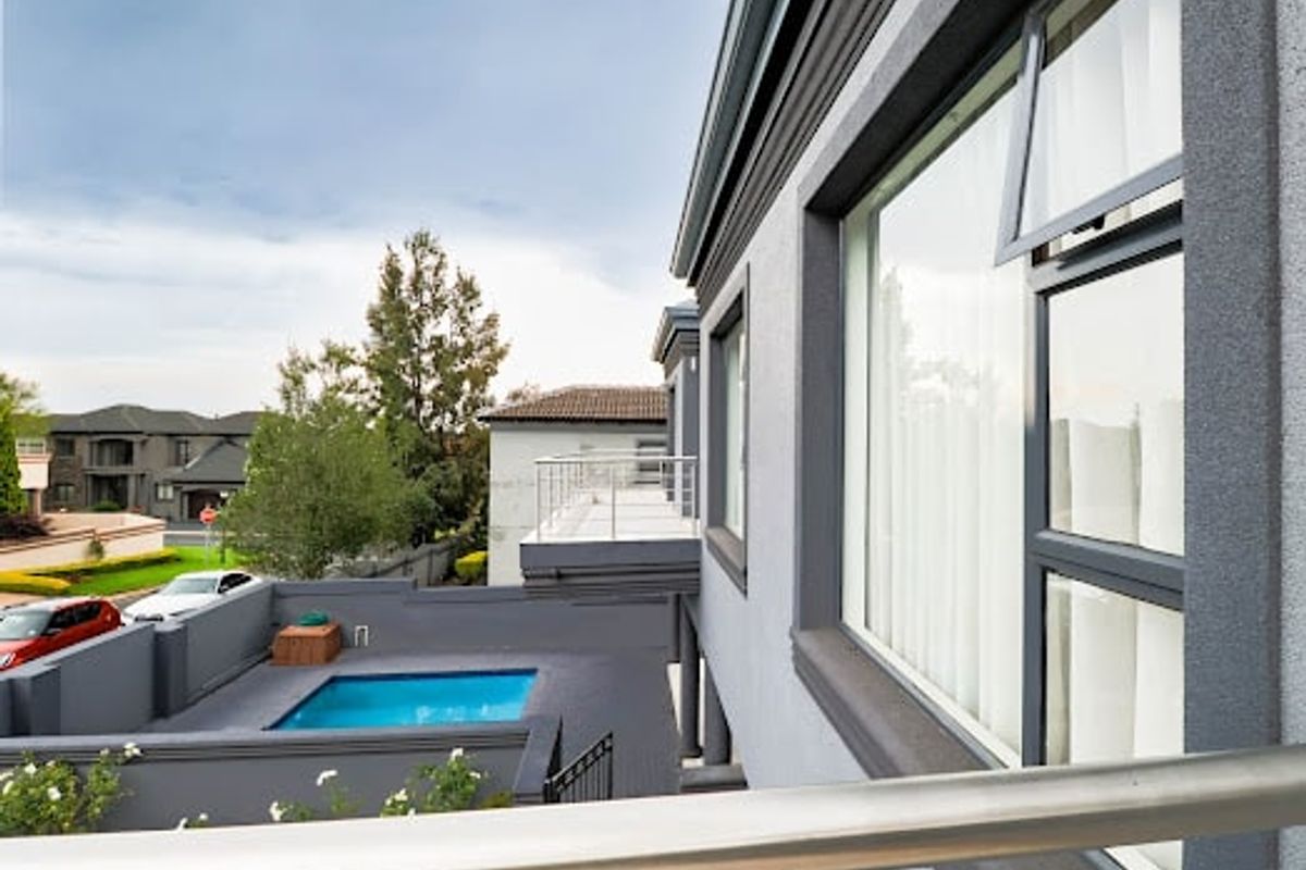 An elevated view of the rear exterior featuring a swimming pool, balcony with metal railings, and modern grey plastered facade.