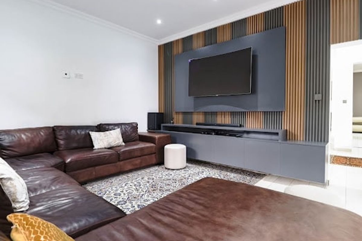 Modern living room featuring a custom built-in media console and a stylish slatted timber and grey feature wall with recessed lighting.