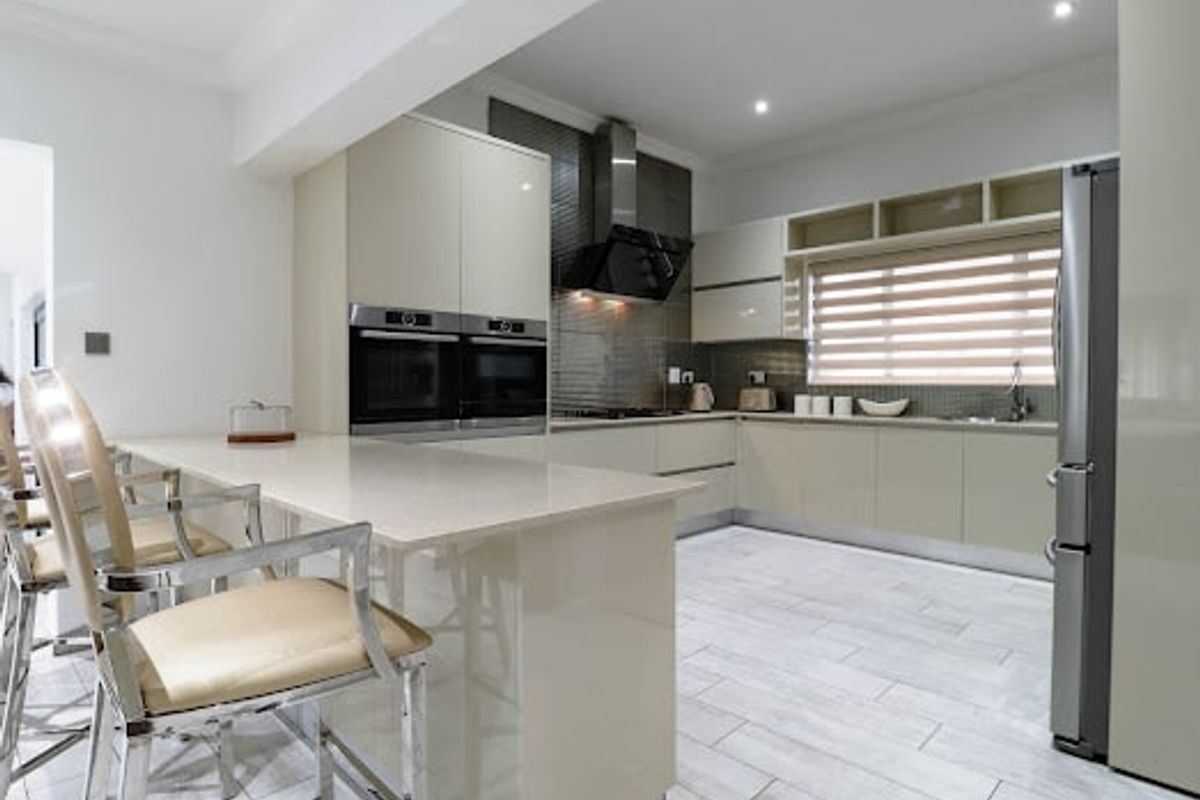Modern kitchen featuring high-gloss cabinetry, built-in double ovens, stone countertops, and a breakfast bar, finished with contemporary tiled flooring and recessed lighting.