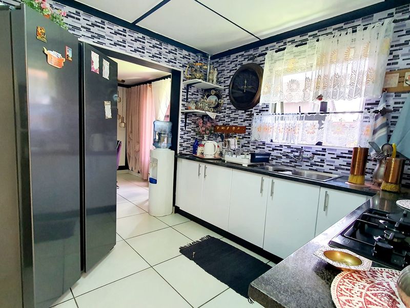 A functional kitchen featuring white cabinetry, a gas hob, stainless steel sink, and a decorative tiled backsplash.