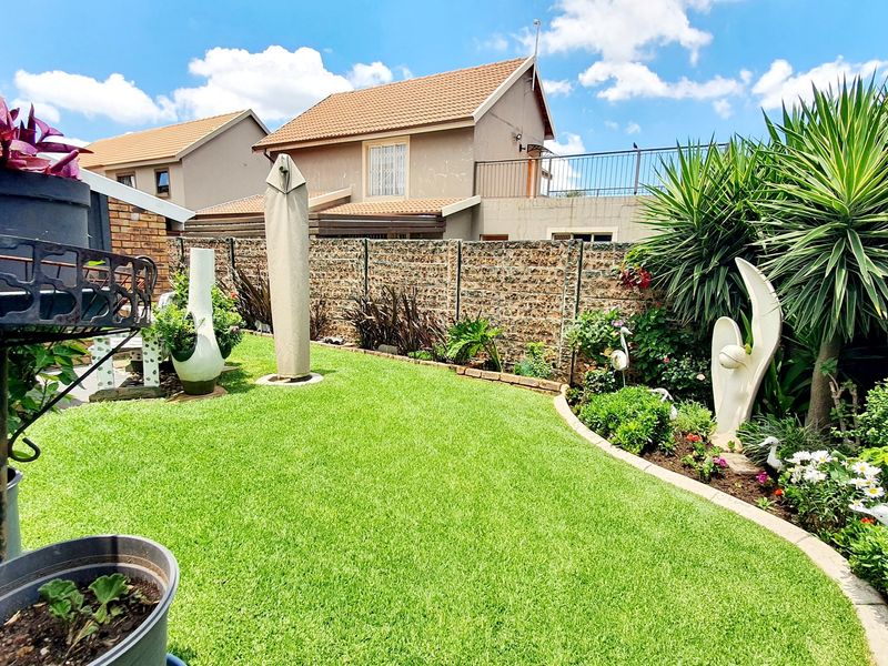 A well-maintained private garden featuring a lush green lawn, landscaped garden beds with concrete edging, and a secure precast concrete boundary wall.