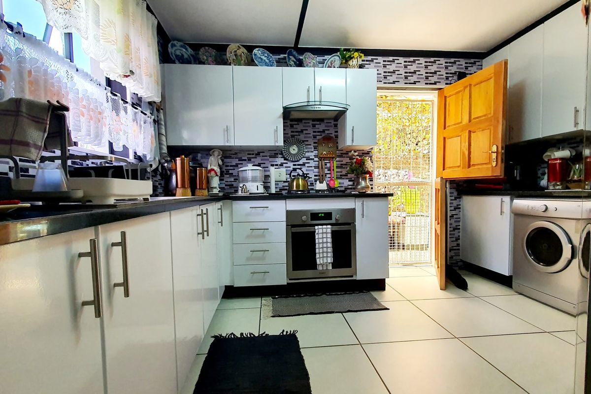 A functional kitchen featuring white cabinetry, built-in oven, extractor fan, tiled splashback, and direct access to the exterior via a stable door.