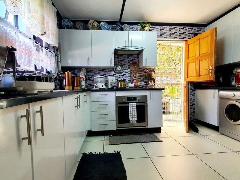 A functional kitchen featuring white cabinetry, built-in oven, extractor fan, tiled splashback, and direct access to the exterior via a stable door.