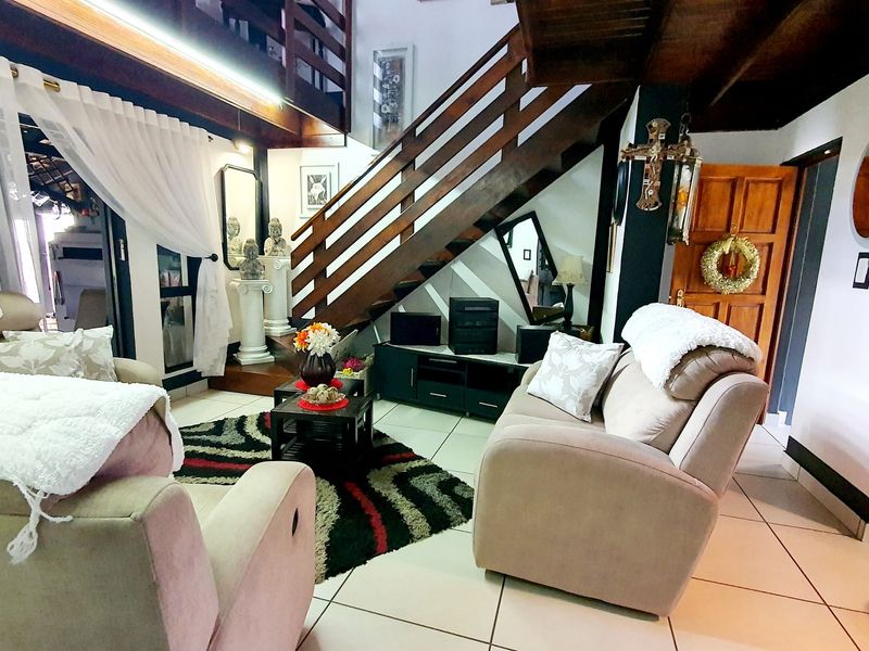A cozy living room featuring a prominent wooden staircase, tiled flooring, and exposed timber ceiling beams, creating a warm and rustic atmosphere.