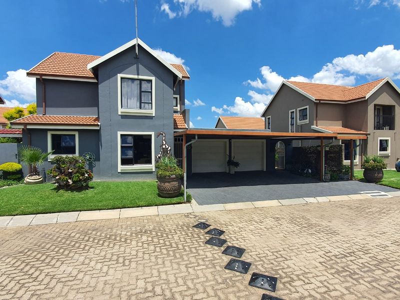 Front view of a double-story residential house featuring a paved driveway, attached carport, double garage, and well-maintained garden.