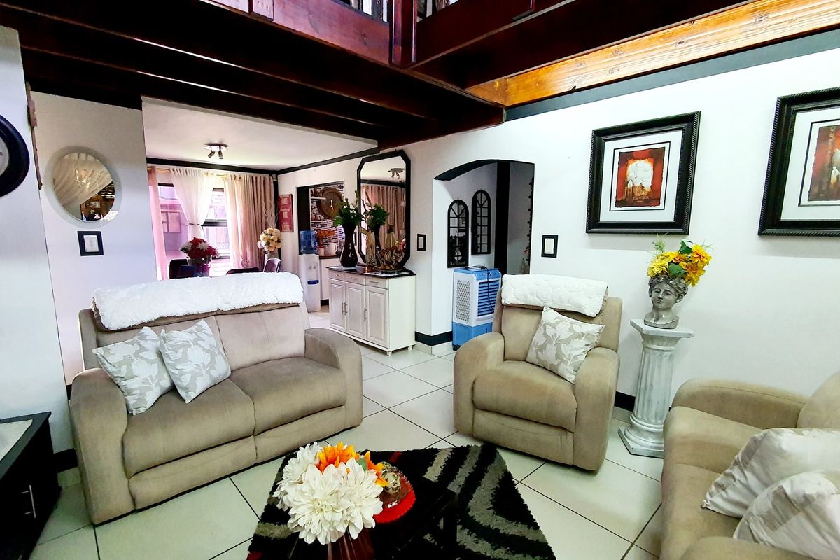 A comfortable living room featuring exposed timber ceiling beams, tiled flooring, and an open-plan layout leading to adjacent living spaces.