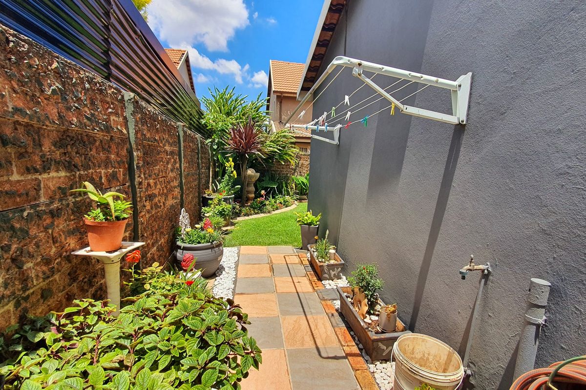 A well-maintained side garden path featuring a tiled walkway, brick boundary wall, and a wall-mounted clothesline, leading to a lush green rear garden area.