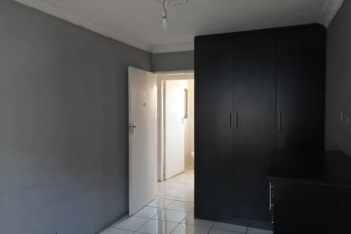 A bedroom featuring tiled flooring, built-in dark cabinetry, and decorative ceiling coving, leading into an adjacent bathroom area.