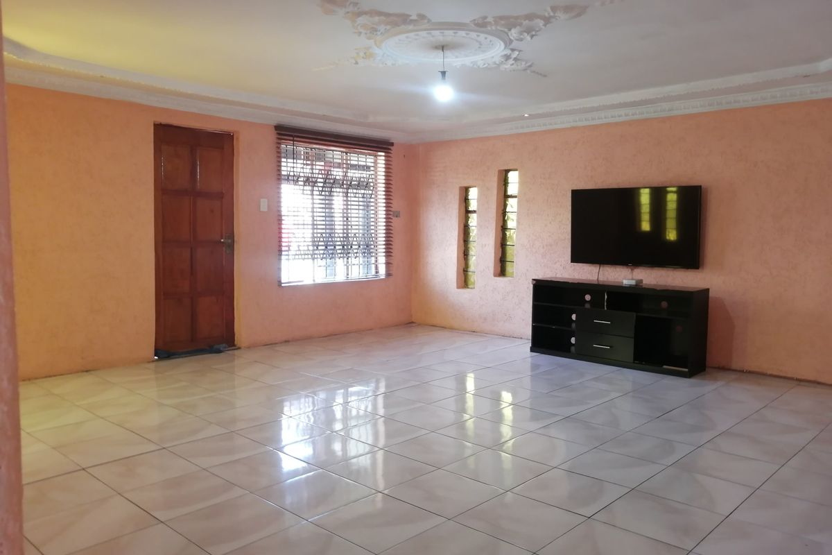 Spacious living room featuring tiled flooring, decorative ceiling detailing, and security bars on the windows.