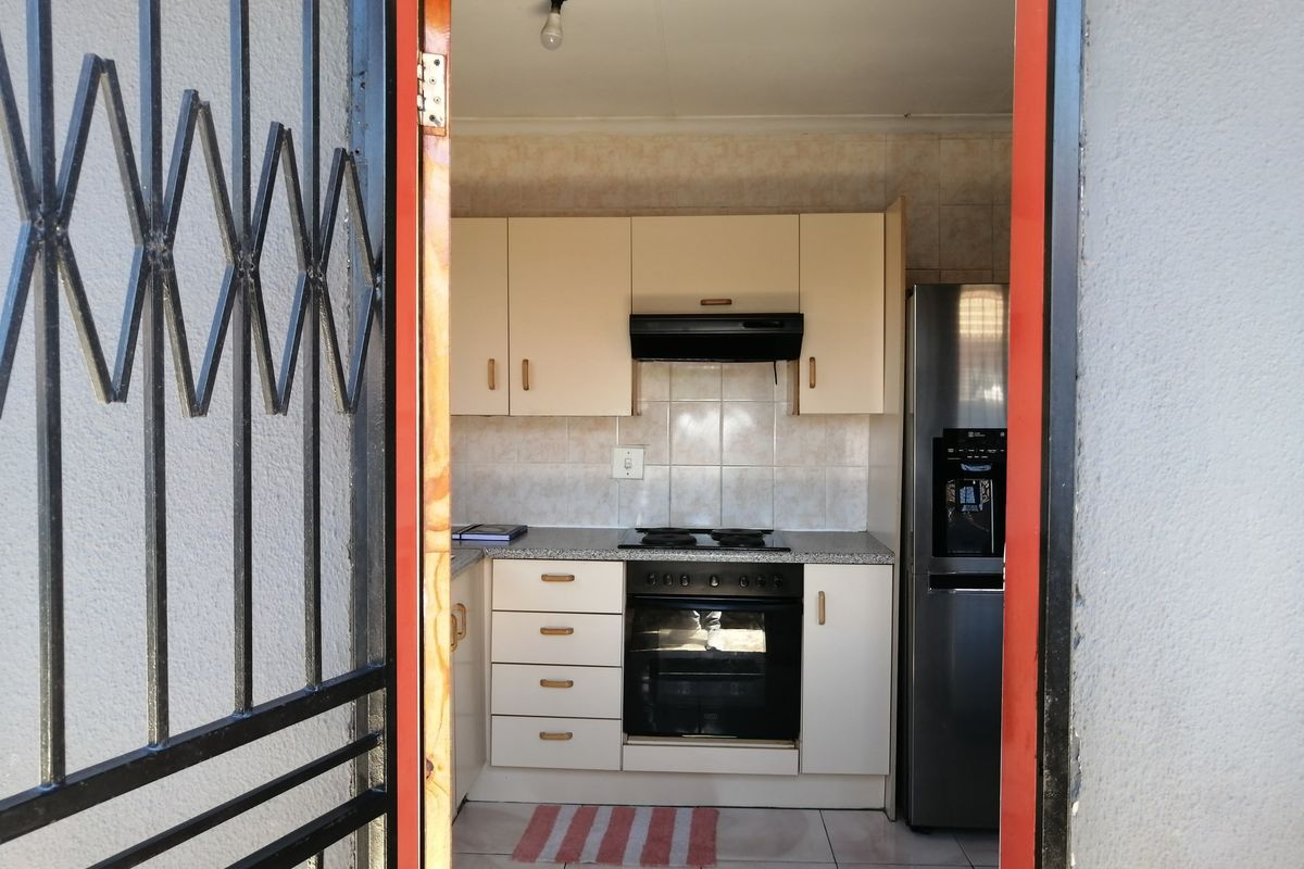A functional kitchen featuring built-in cabinetry, an integrated oven and hob, extractor fan, and tiled splashbacks, viewed through a security gate entrance.