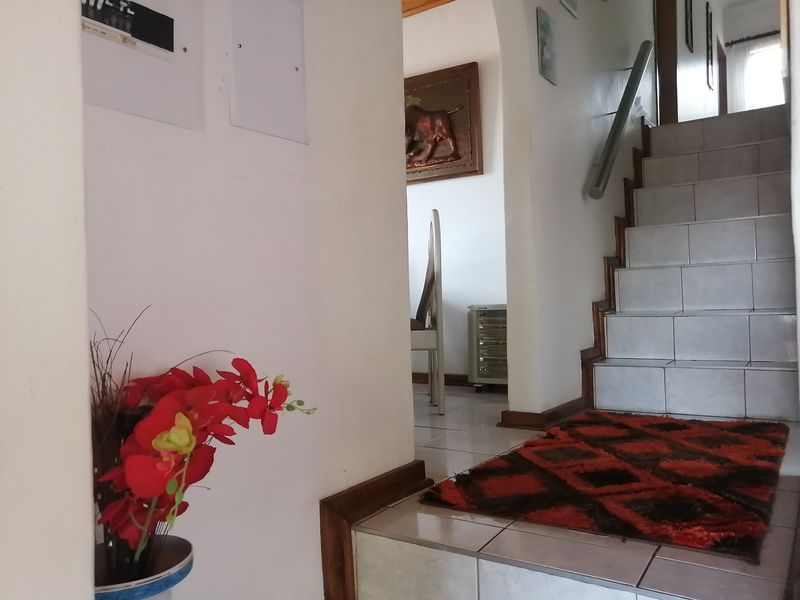 A tiled hallway featuring a staircase with a metal handrail, leading through an archway into an adjacent living space.