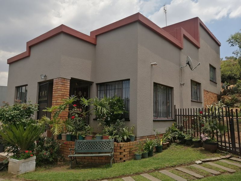 A well-maintained two-story house featuring a textured grey facade with brick accents, security window bars, and a landscaped front garden area.