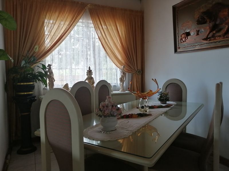 A dining room featuring tiled flooring and a window fitted with security bars, offering a functional space for family meals.