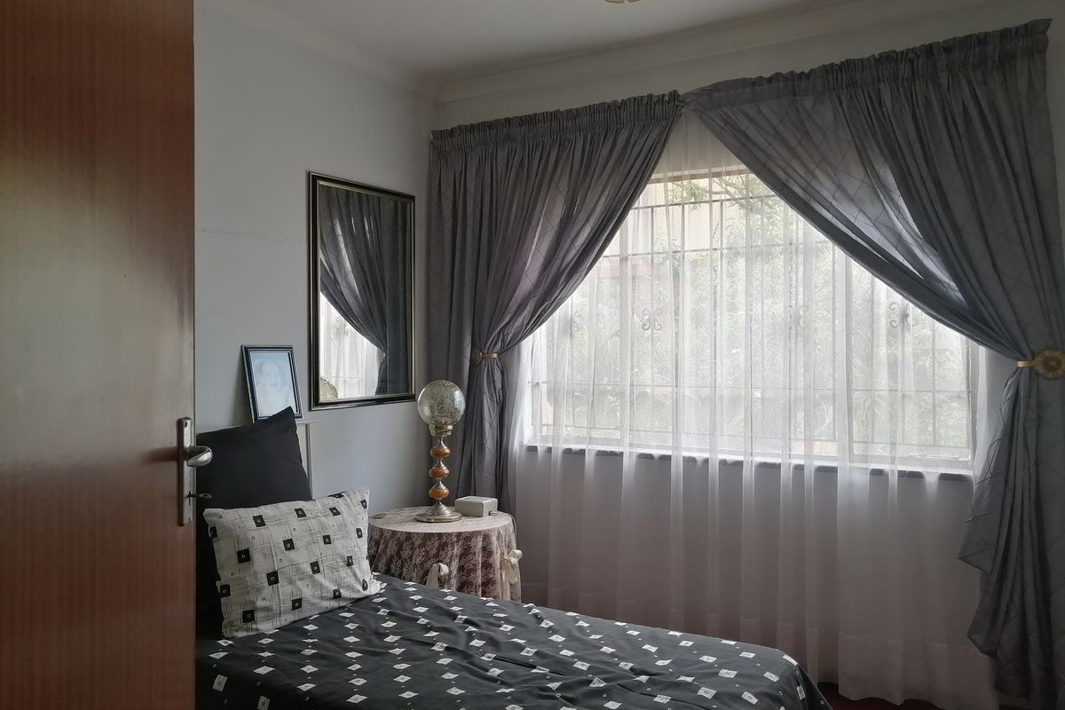 A functional bedroom featuring a window with security bars, ceiling cornice, and a central light fixture.