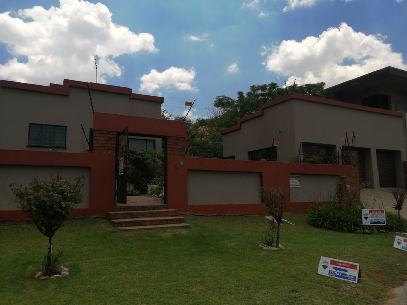 Front view of a residential property featuring a perimeter wall with electric fencing, a brick entrance gate, and a paved walkway leading to the house.